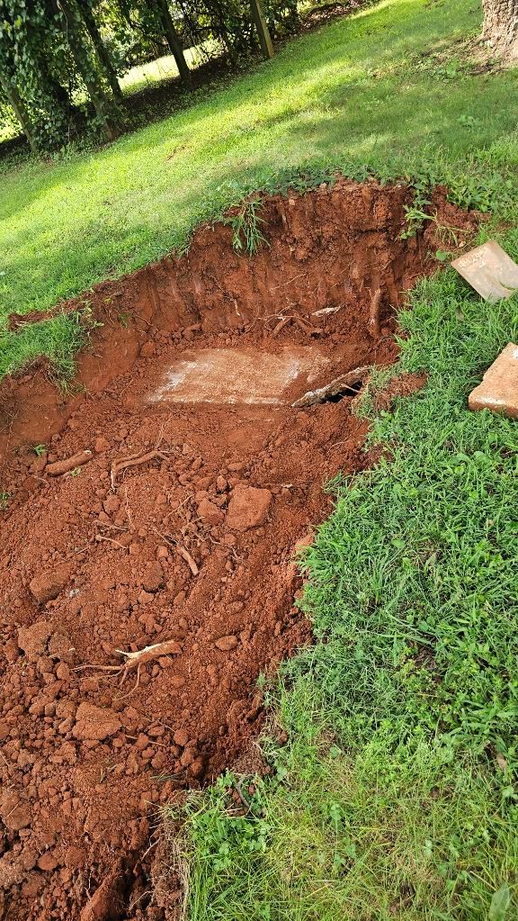 Freshly dug trench in a grassy yard with exposed red soil and scattered dirt