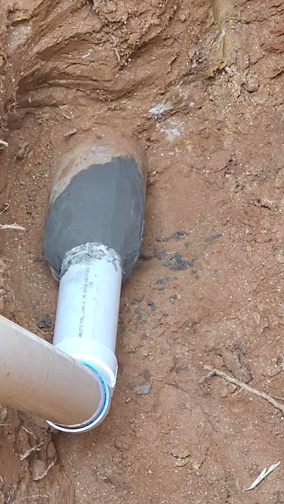 White pipe joint sealed with gray foam in a dirt trench