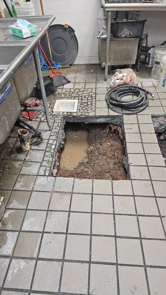 Broken patio tiles with a large hole exposing dirt and debris near outdoor equipment and coiled hose