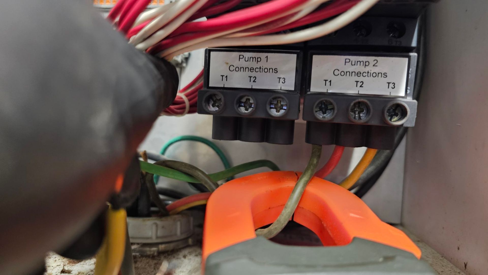 Close-up of electrical wiring with labeled terminal blocks and orange cable clamps inside a panel