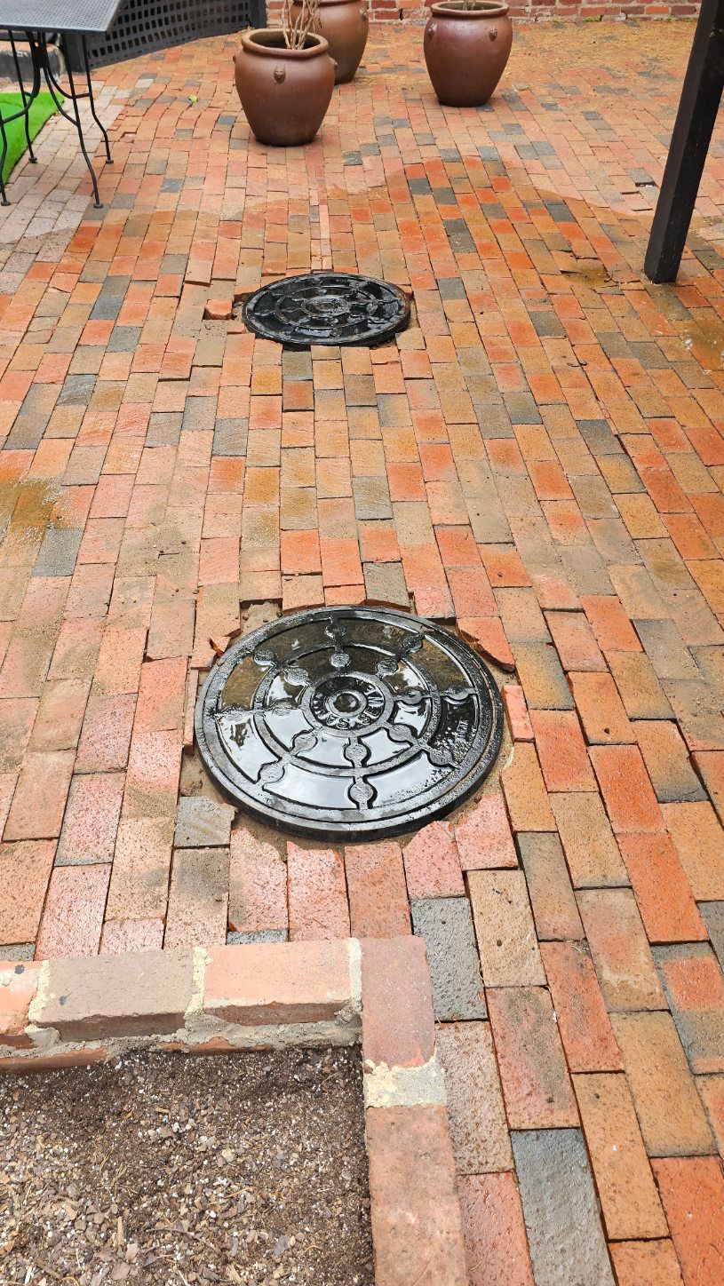 Brick patio with two round manhole covers and potted plants in the background