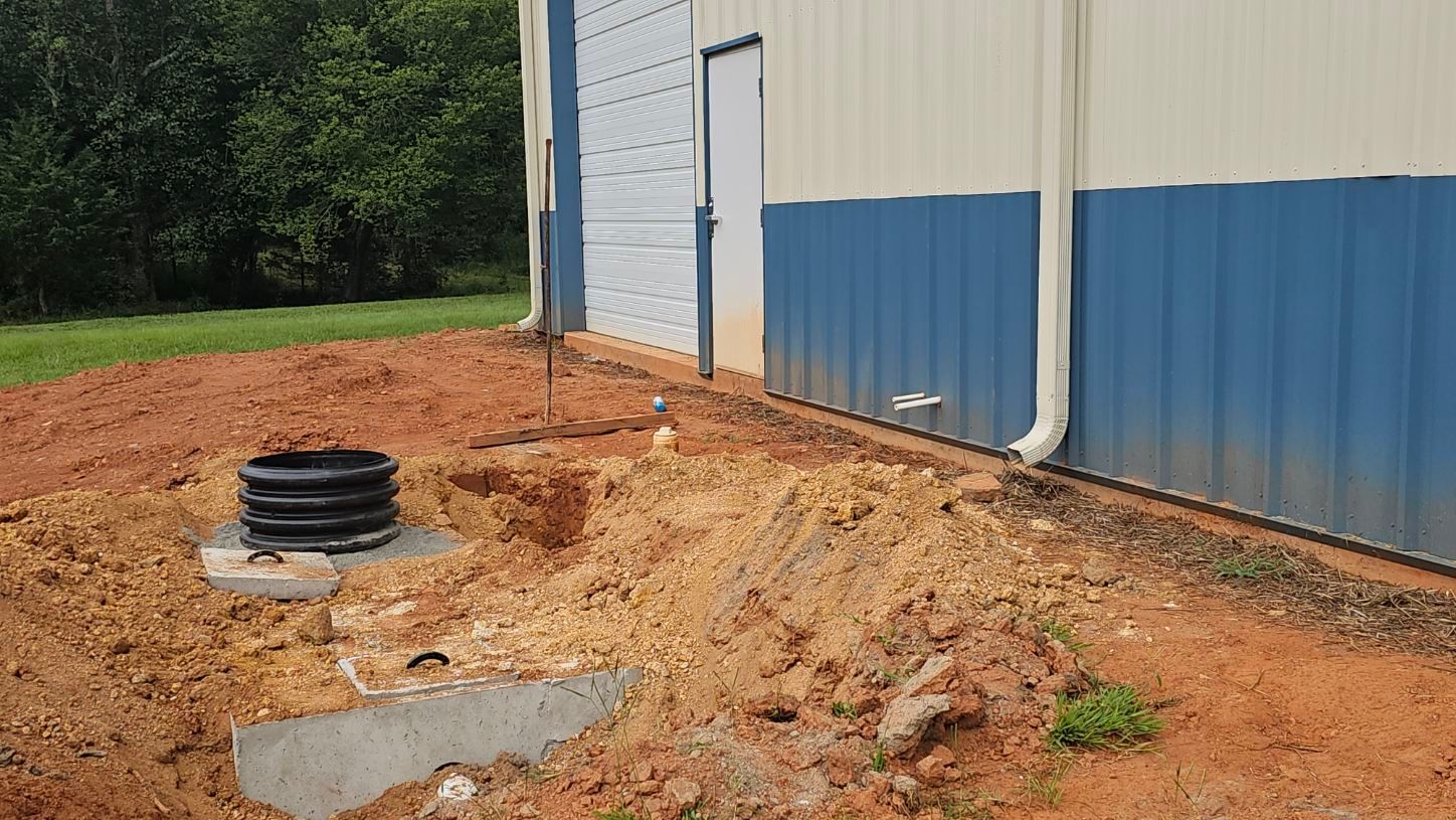 Blue-and-white building beside a dirt lot with a black vent pipe and exposed ground utilities.