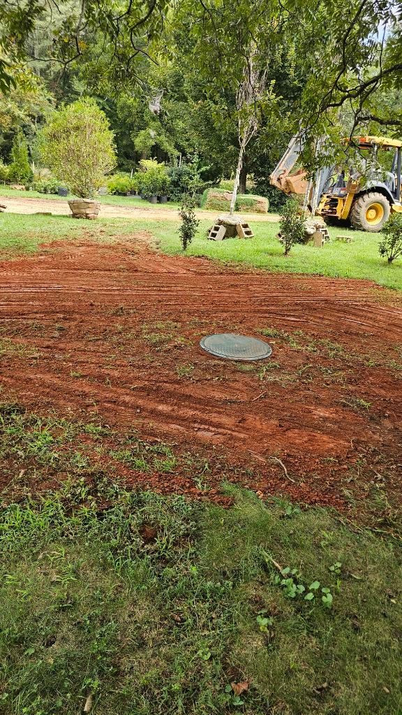 Reddish dirt-covered yard with trees and a tractor in the background