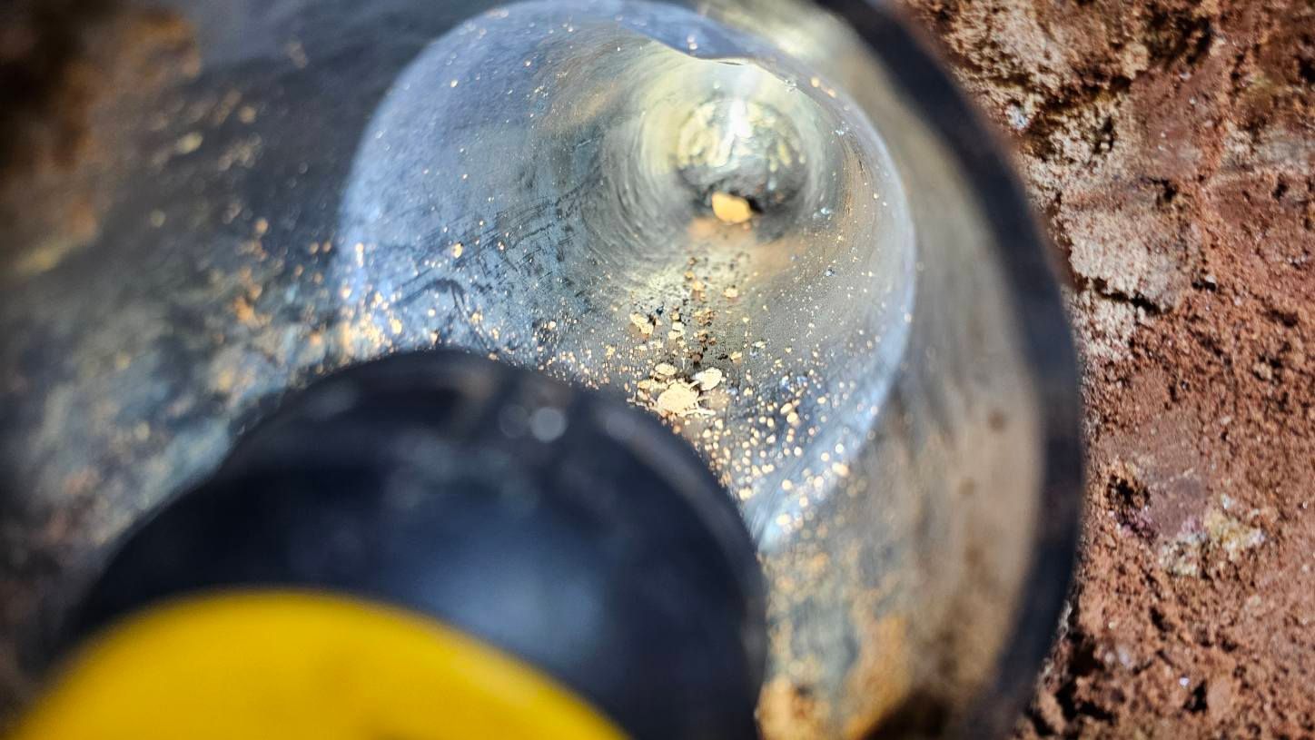 A yellow flashlight beam illuminates a clear glass bulb embedded in dirt.