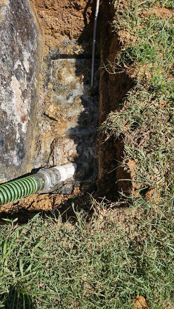 Green hose draining muddy water from a small trench beside grass and dirt.