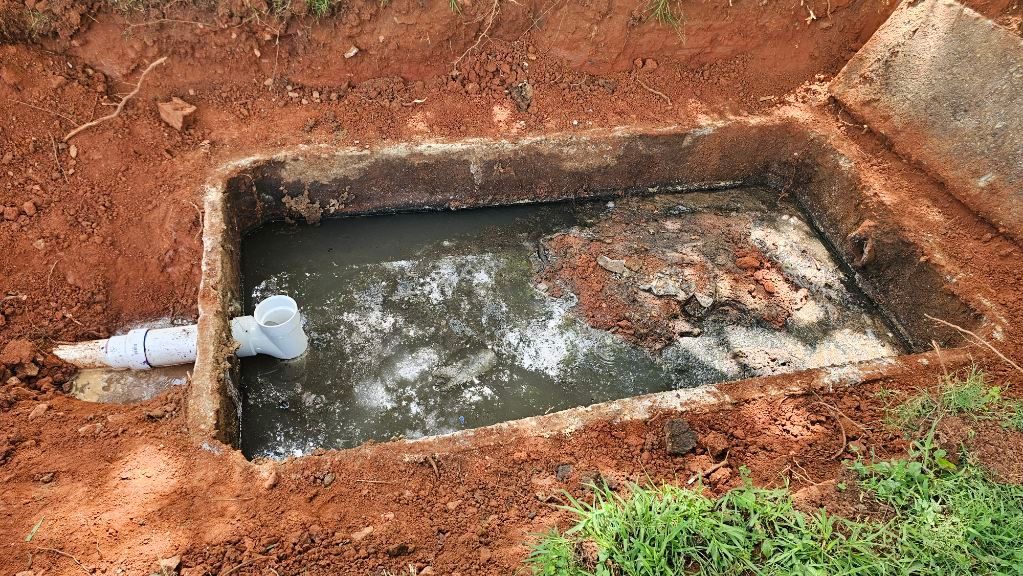 Water-filled concrete tank set in red dirt, with a white pipe entering from the left.