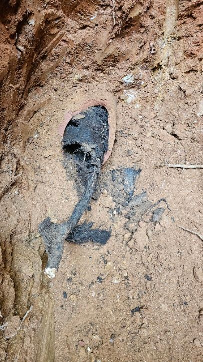 Black cable or pipe exposed in a muddy dirt trench with wet soil around it