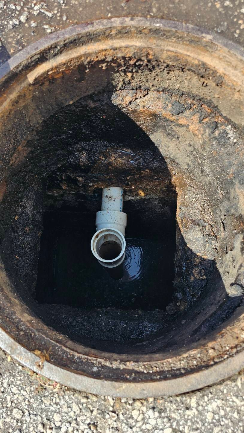 Open manhole showing a rusted pipe opening inside a circular concrete chamber.