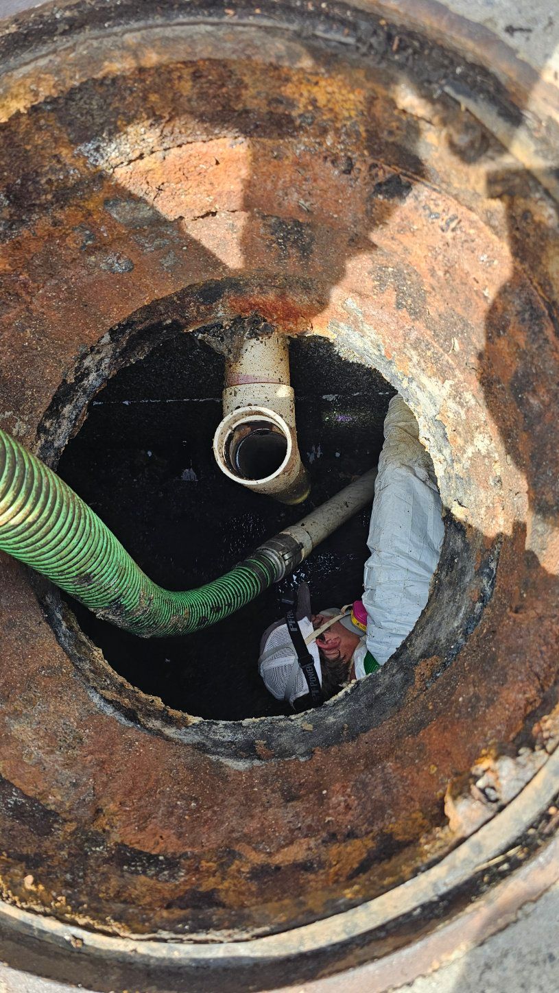 Rusty circular manhole opening with pipes and a green hose inside