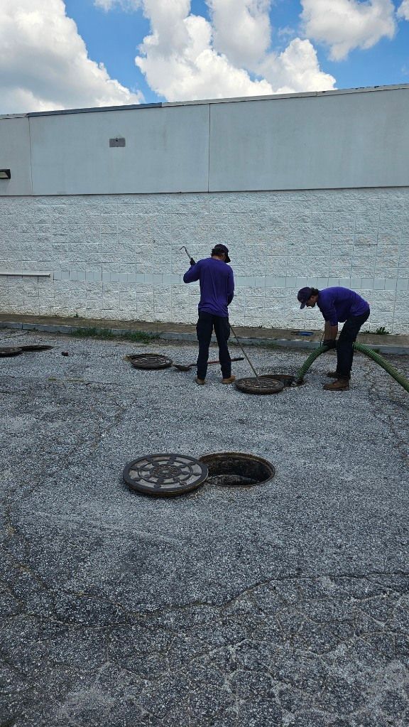 Two workers in purple jackets inspect rooftop gravel near a white wall under a cloudy sky
