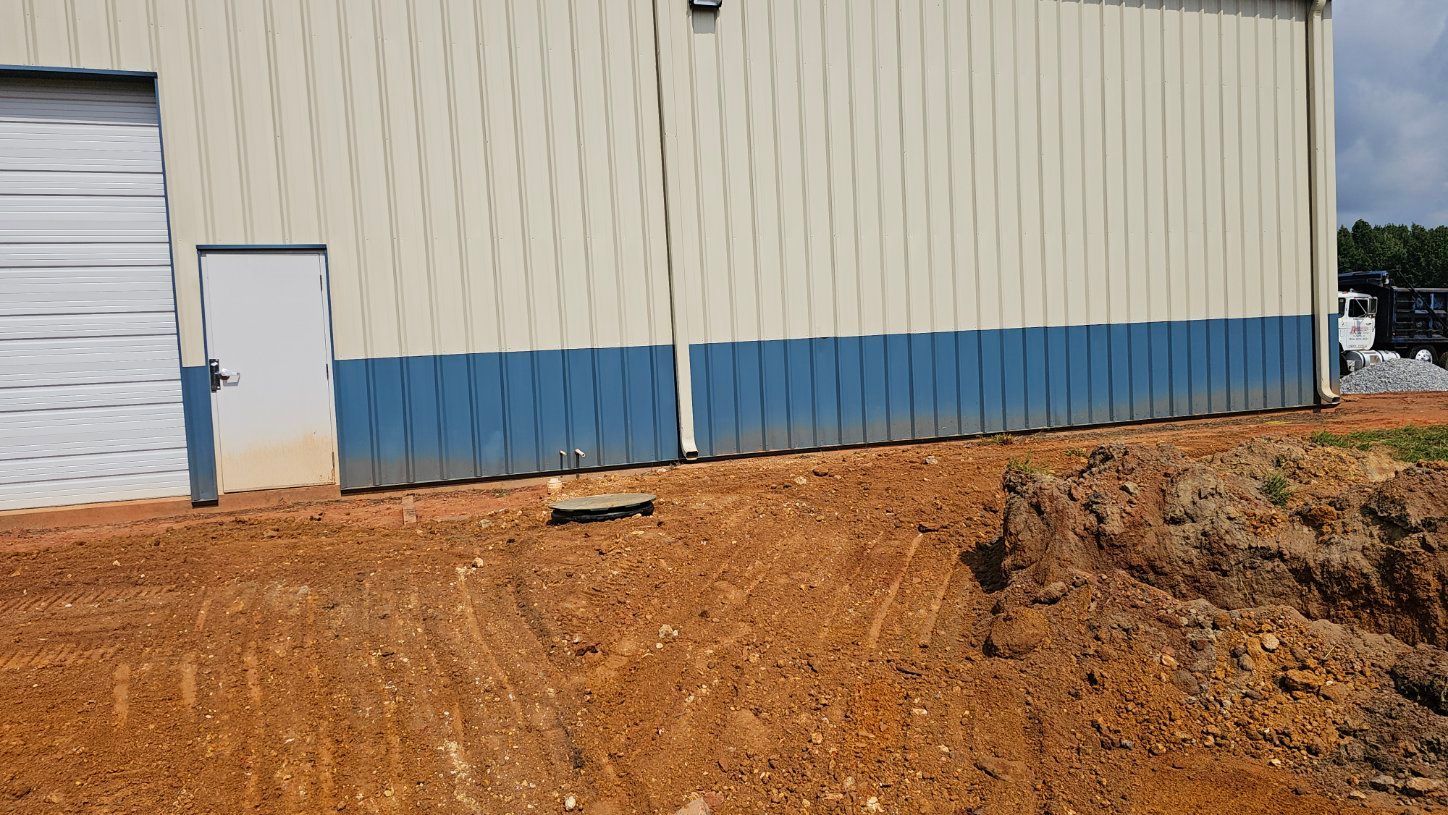 Beige and blue industrial building with a white door beside a reddish dirt lot.