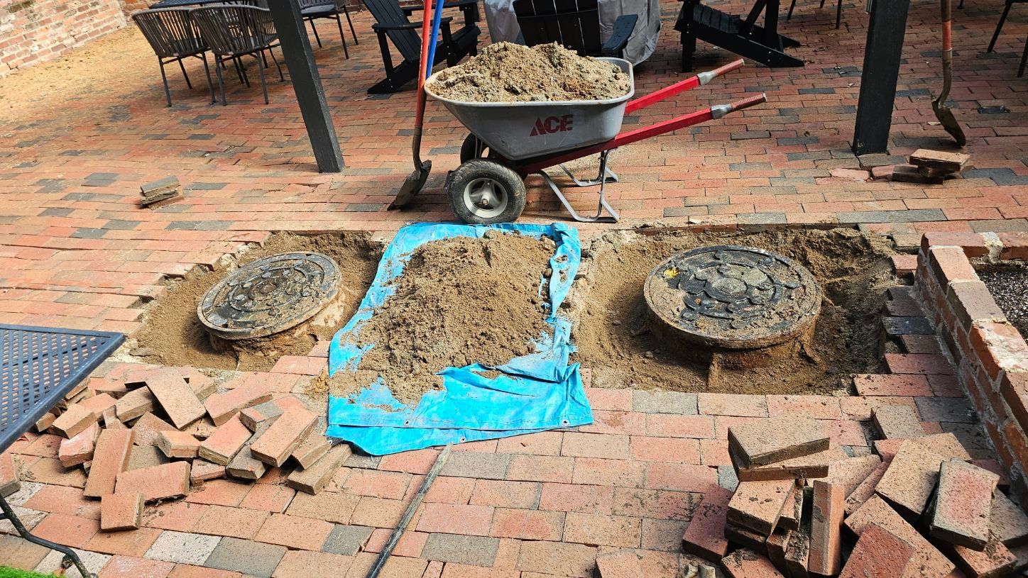 Wheelbarrow and piles of wet concrete on a brick patio, with blue tarp and scattered bricks.