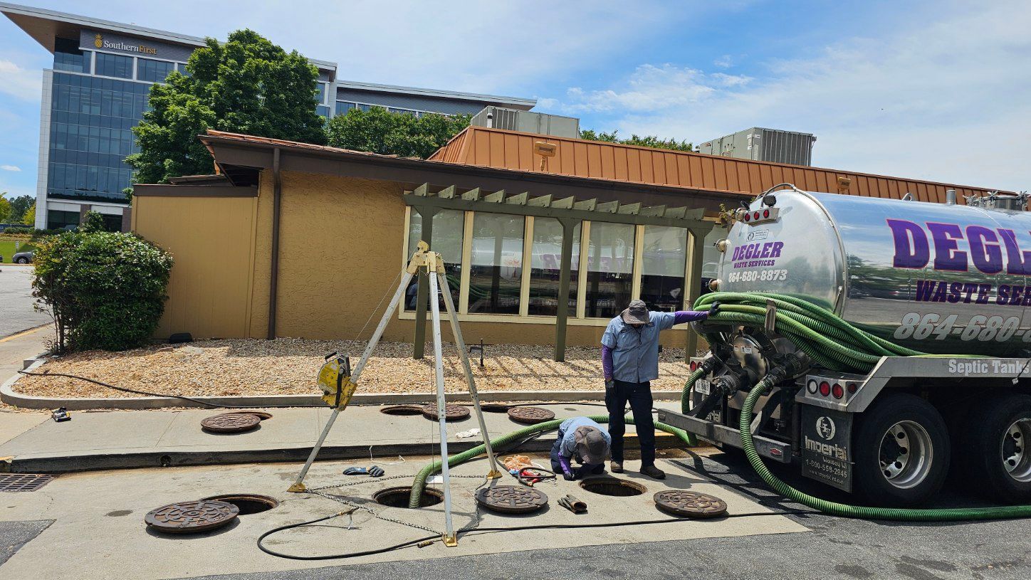 Worker on sidewalk near a cement mixer truck and hoses outside a small building under clear blue sky