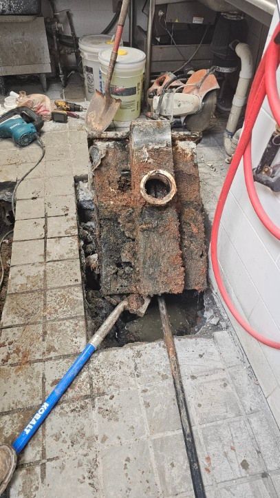 Rusty industrial machine on tiled floor beside a blue pole and red hose in a cluttered workspace