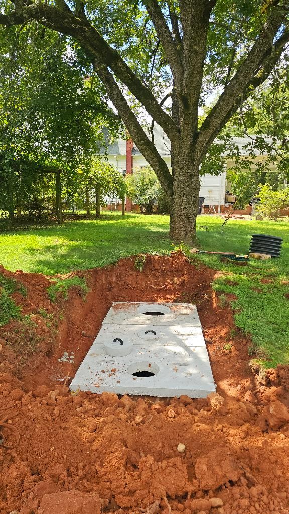 Concrete utility slab in a red-soil trench beneath a large tree in a grassy yard