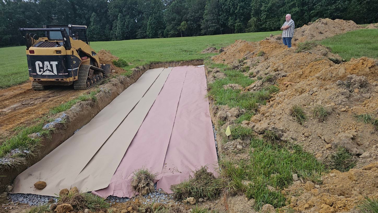 Construction site with a CAT skid steer beside a long trench covered by pink and tan tarps