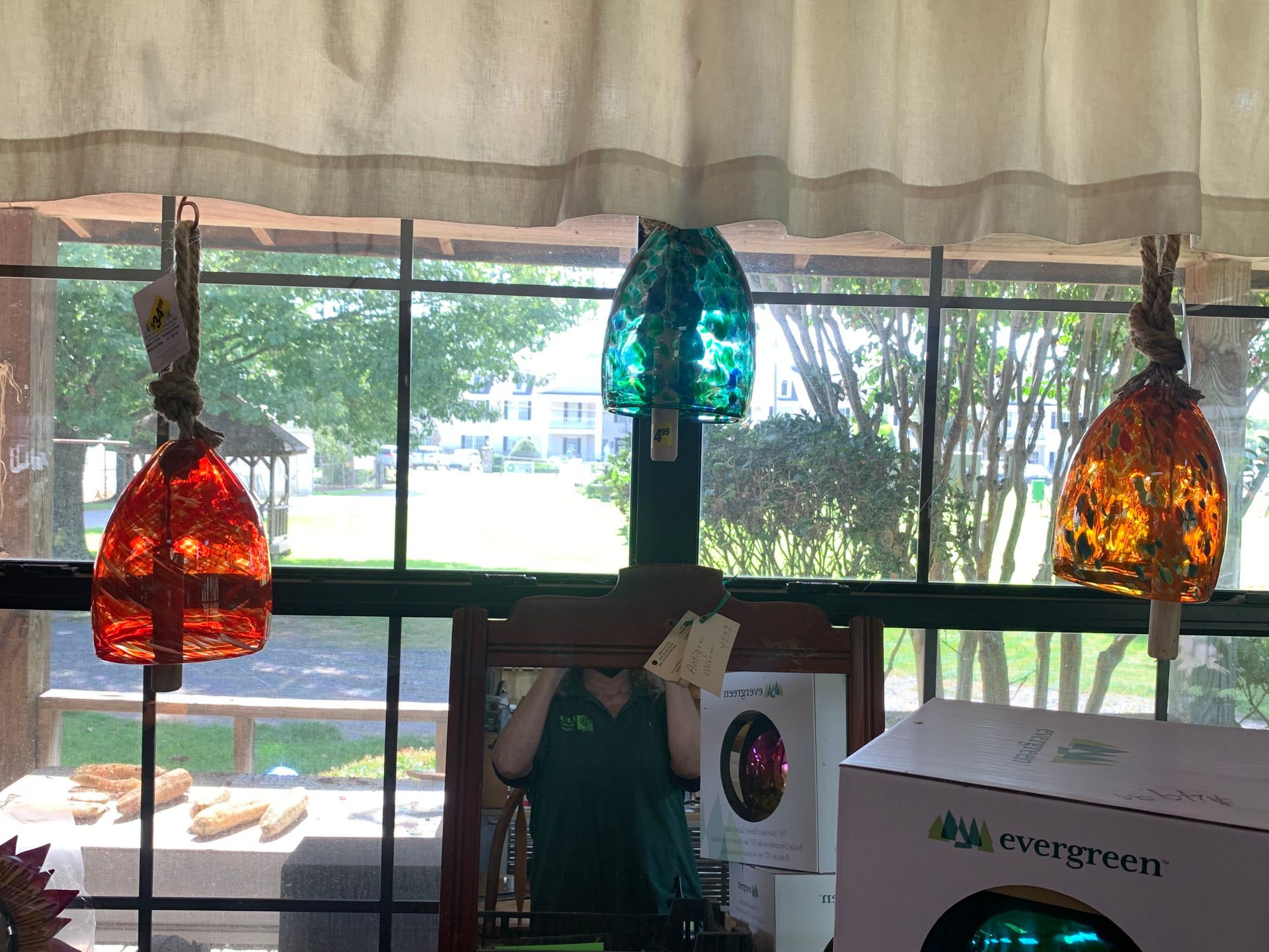 Hanging colorful glass pendant lamps in front of a window with a leafy outdoor view.