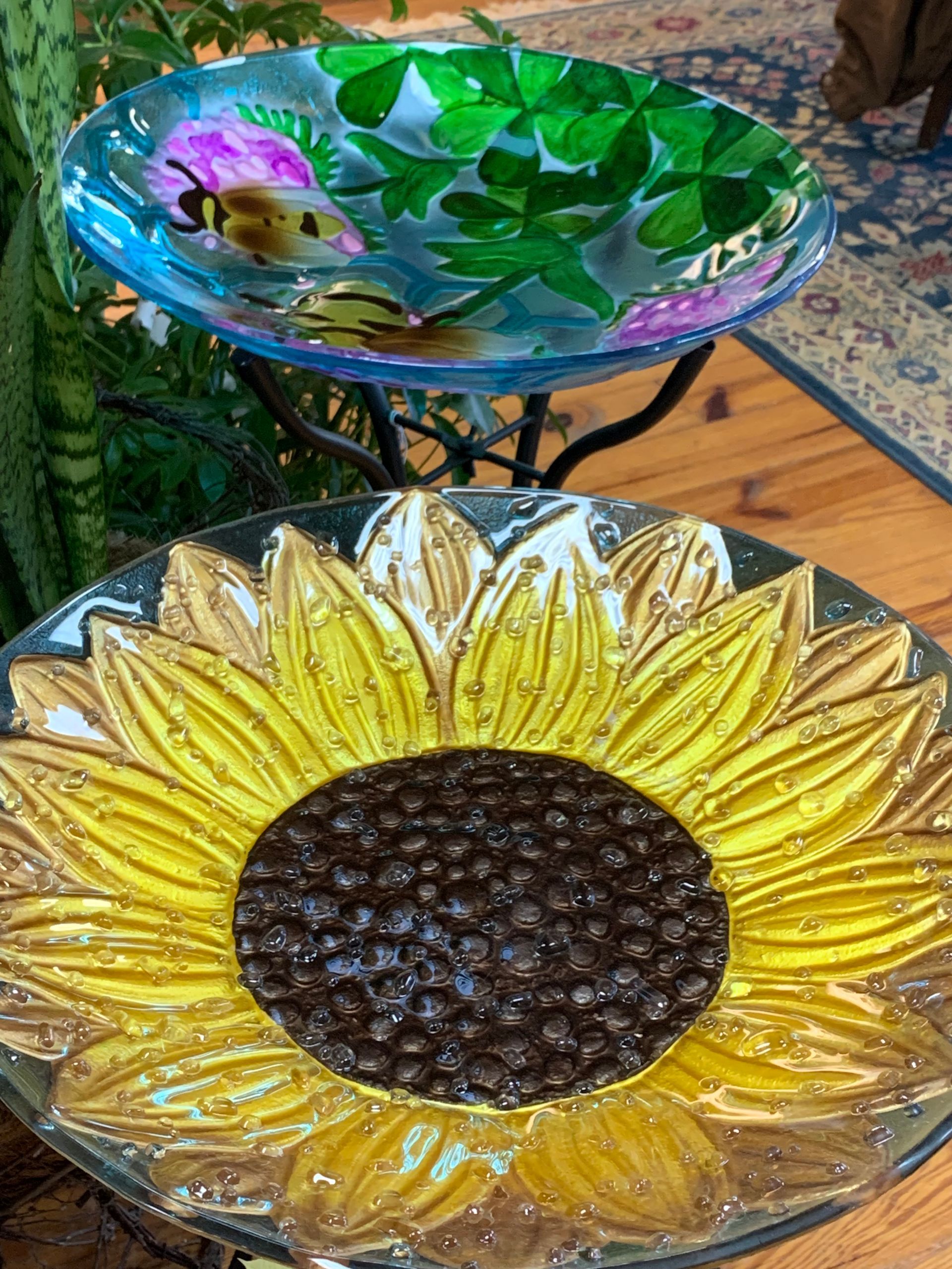 Glass sunflower bowl with yellow petals and dark center, in front of a green glass bowl with a flower