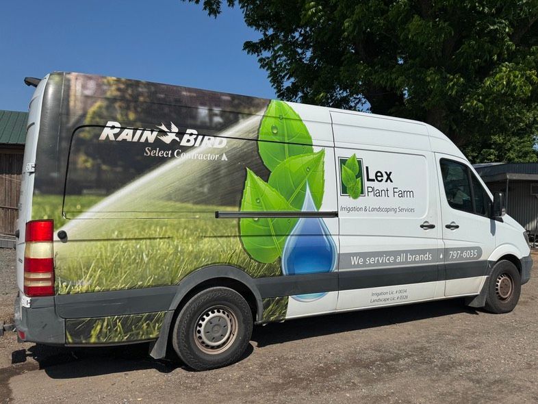White Lex Pest Fan van with green leaf graphics parked outdoors on a sunny day