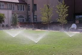 Sprinklers watering a grassy lawn in front of an apartment building