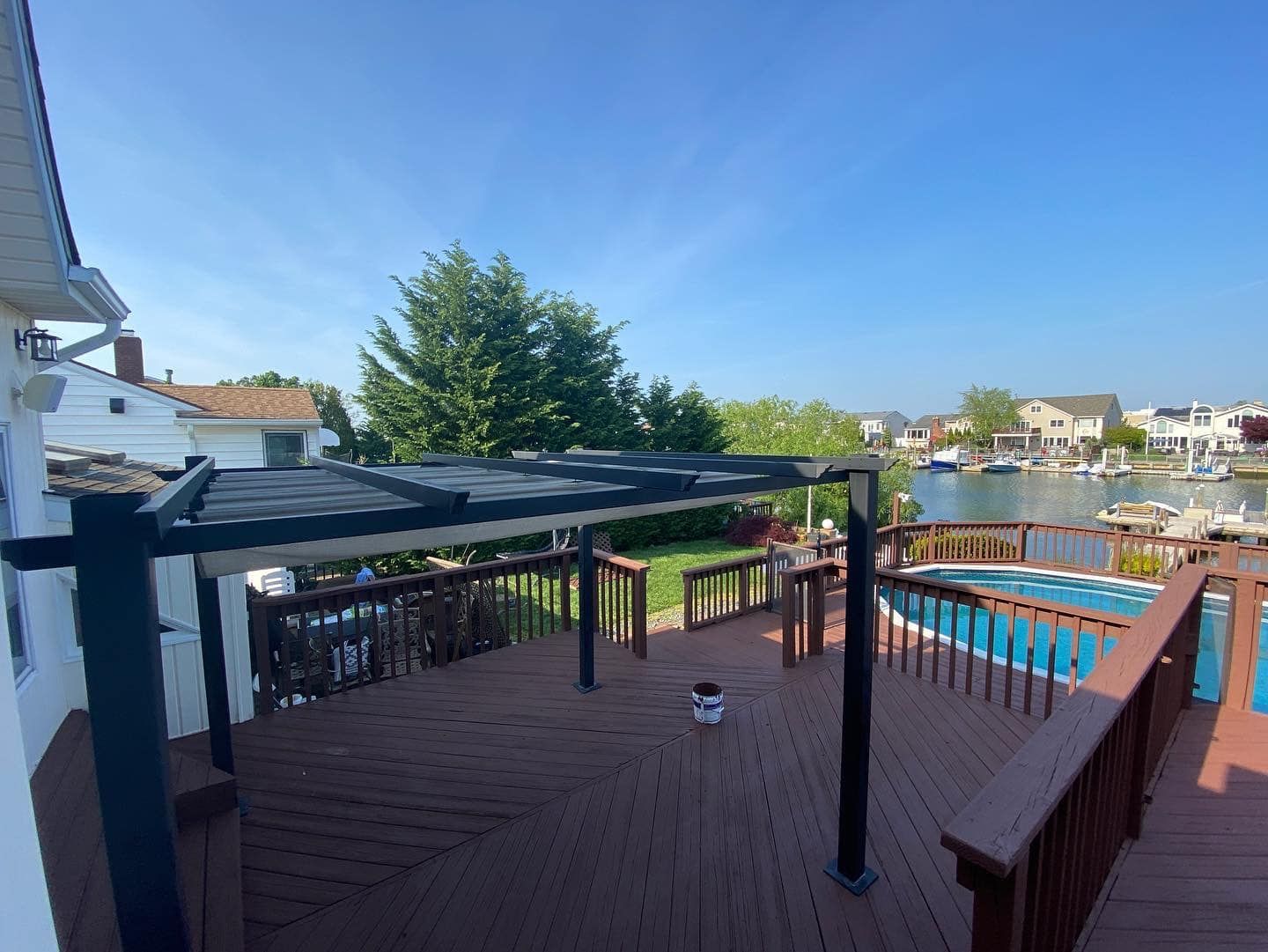 Backyard deck with pergola, railing, and a swimming pool under a clear blue sky