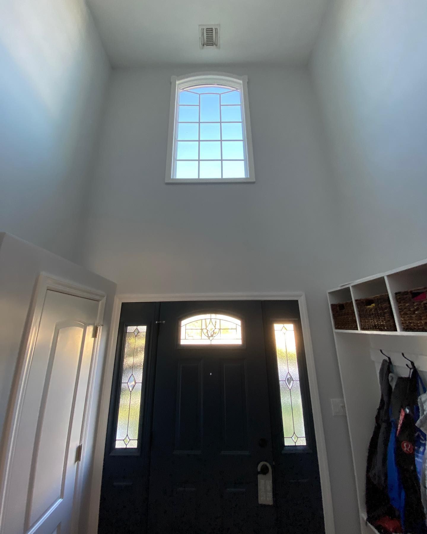 Entryway with white walls, black front door, high window, closet, and hanging coats.