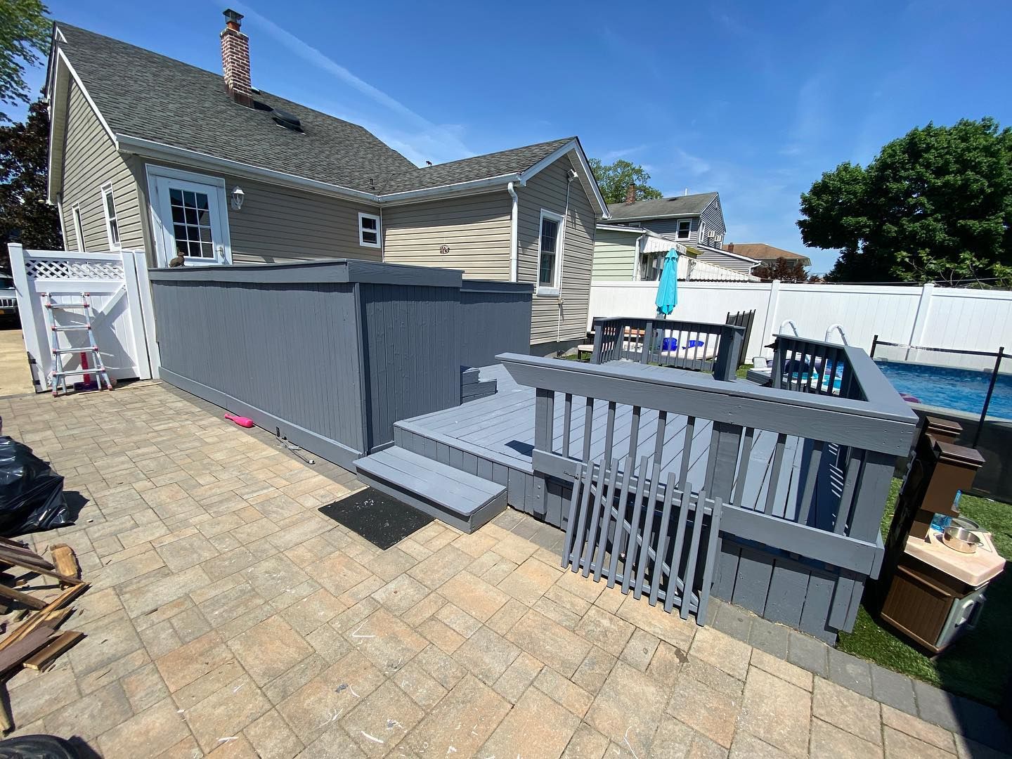 Backyard deck with gray railings and steps beside a house on a sunny day