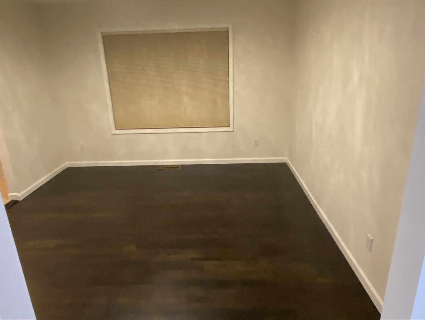 Empty beige room with dark wood floor and a window.