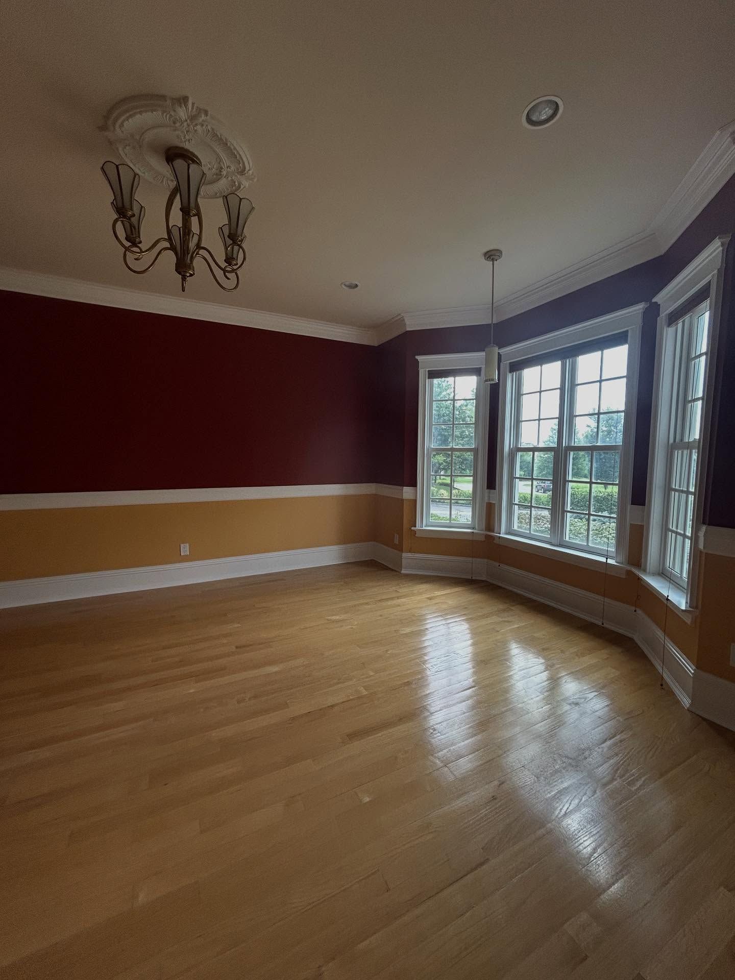 Empty living room with hardwood floors, red accent wall, and bay windows letting in daylight