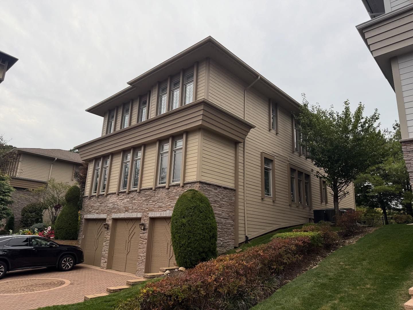 Two-story stone house with garage and driveway on a sloped residential street