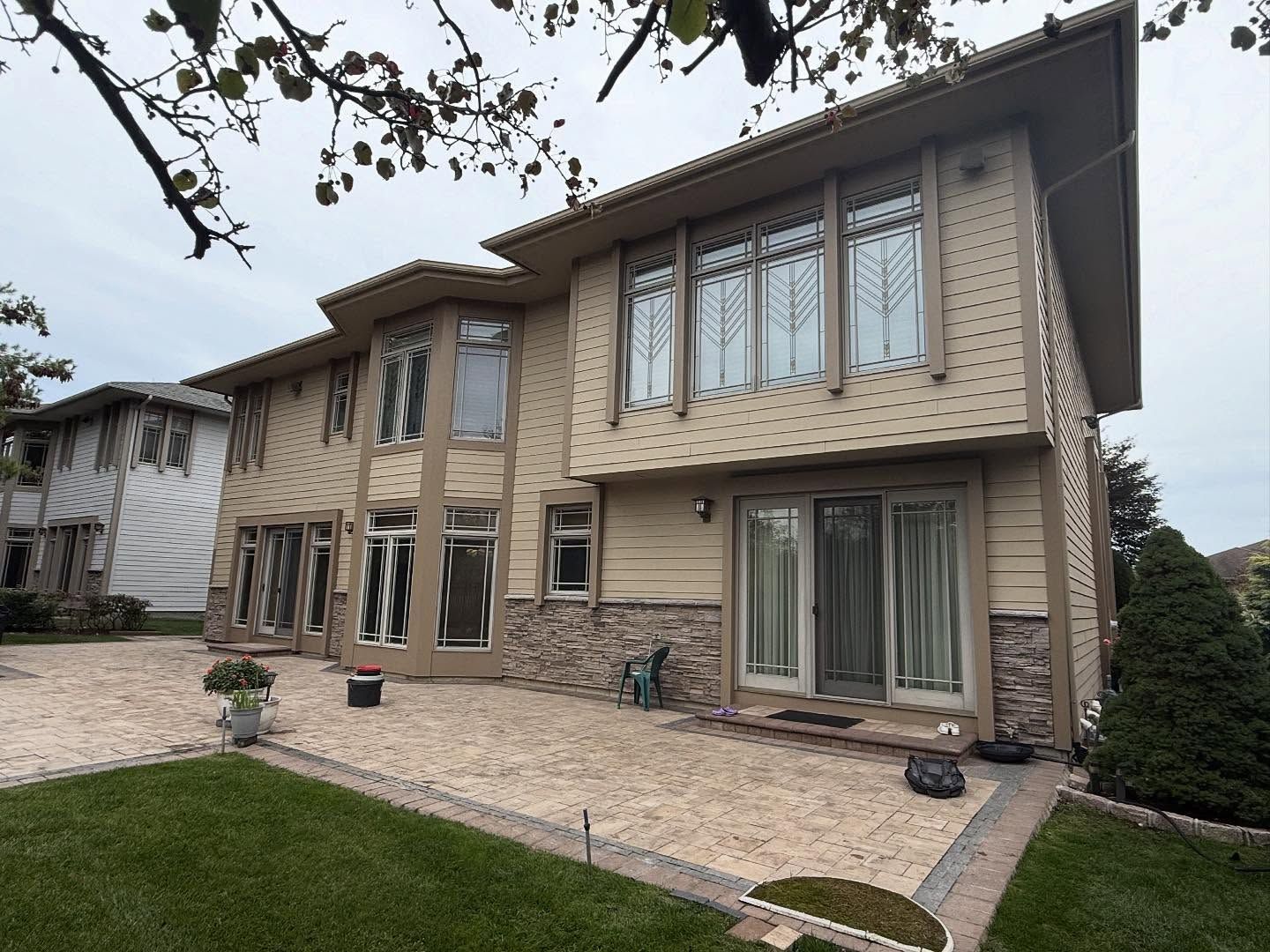 Modern two-story beige house with large windows, patio paving, and a green lawn