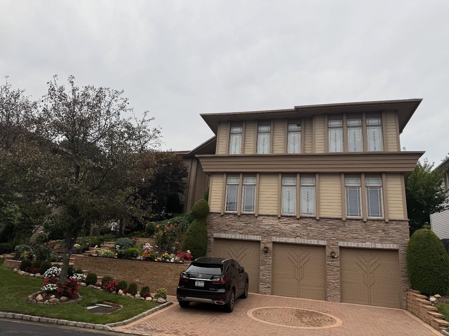 Large two-story brick house with a landscaped front yard and a black car parked in the driveway.