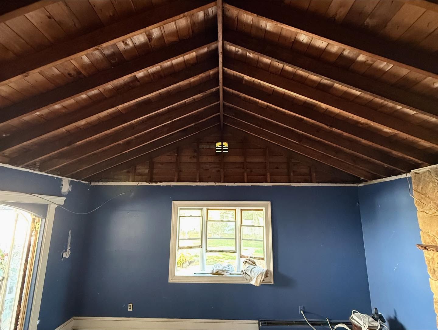 Empty room with exposed wooden rafters, blue walls, and a small window centered on the far wall.