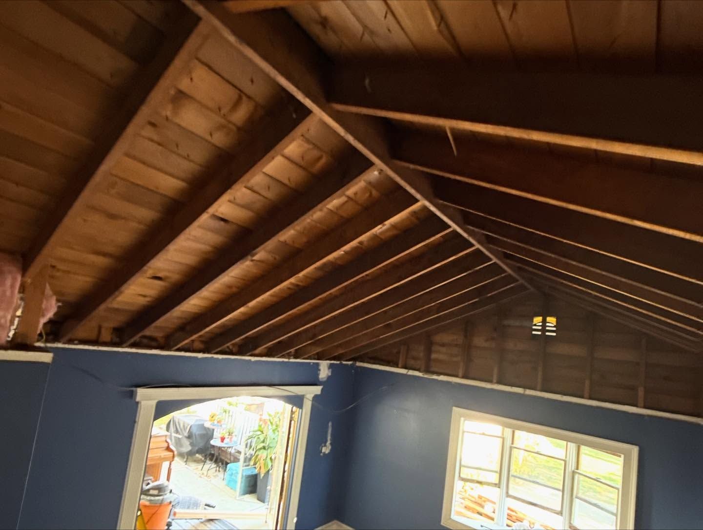 Interior with exposed wooden roof beams over blue walls and a bright doorway and window below