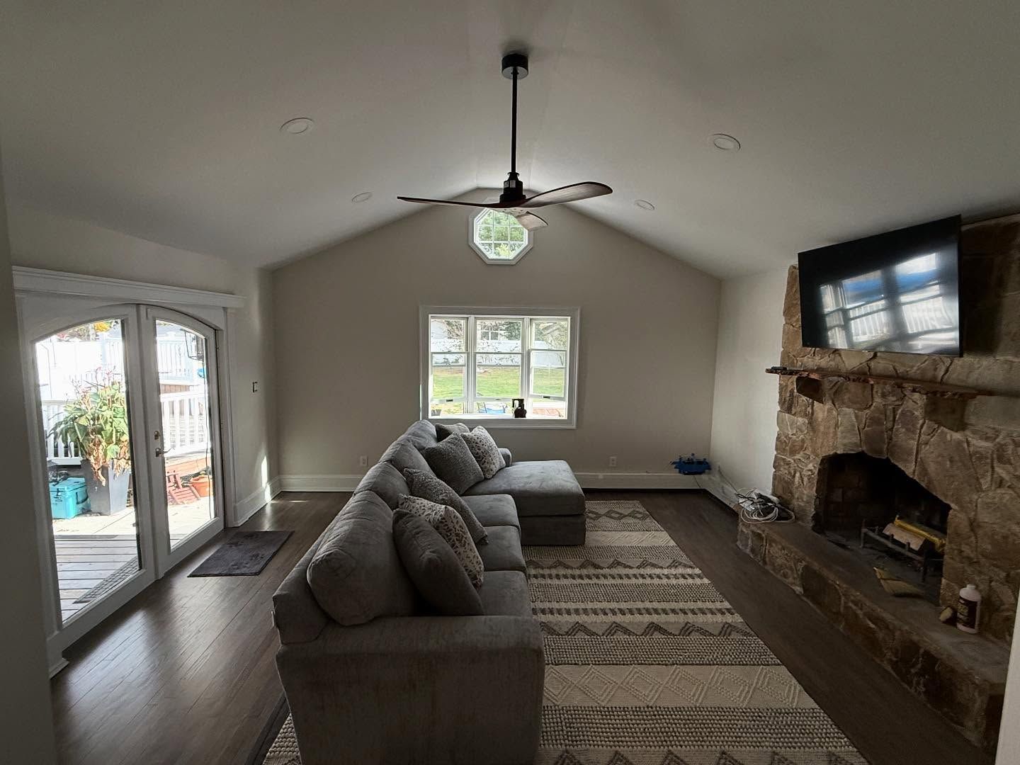 Spacious living room with gray sofa, stone fireplace, ceiling fan, and sliding doors to a patio.