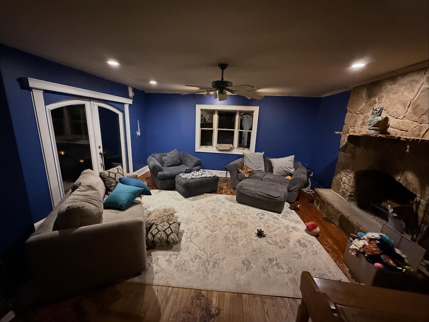 Blue living room with sofas, white rug, ceiling fan, and a stone fireplace on the right