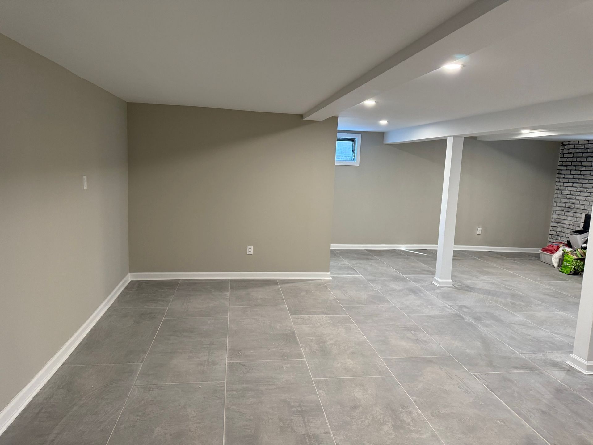 Empty finished basement with gray tile floor, beige walls, white support columns, and recessed lighting
