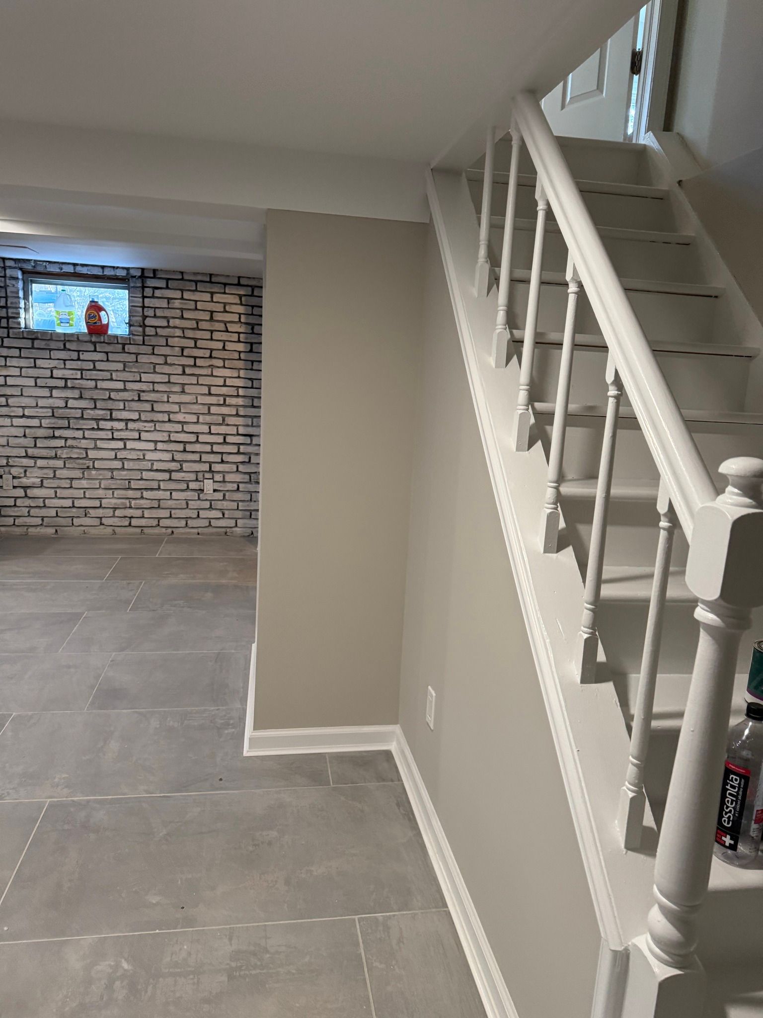 Indoor basement stairway beside a tiled floor and brick accent wall with a wall-mounted TV.