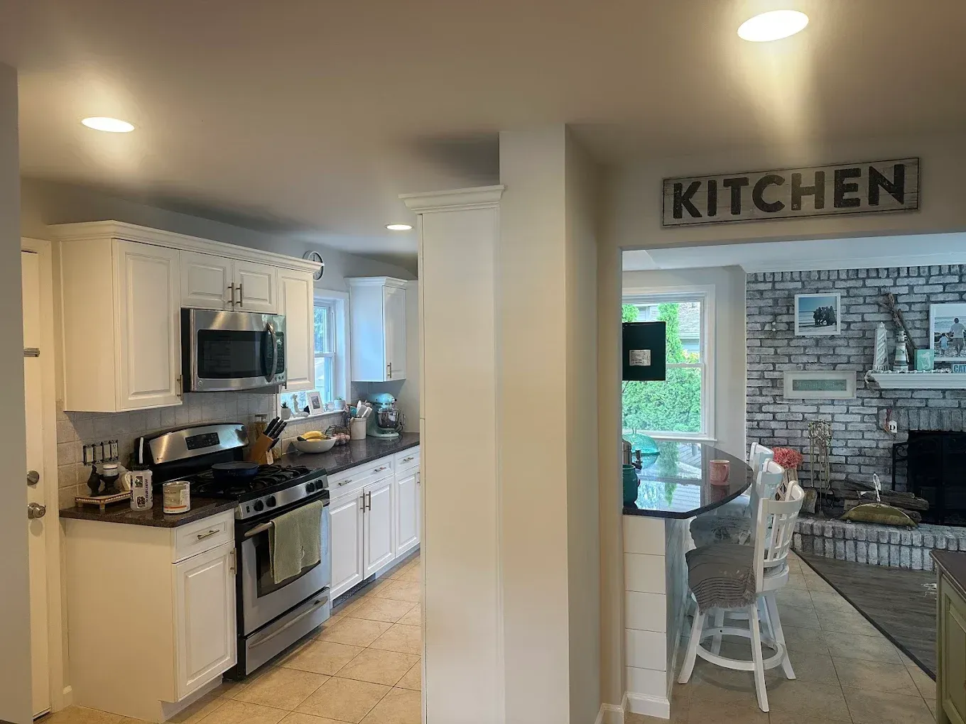 Bright kitchen with white cabinets and stainless steel stove, opening to a living area labeled “KITCHEN”