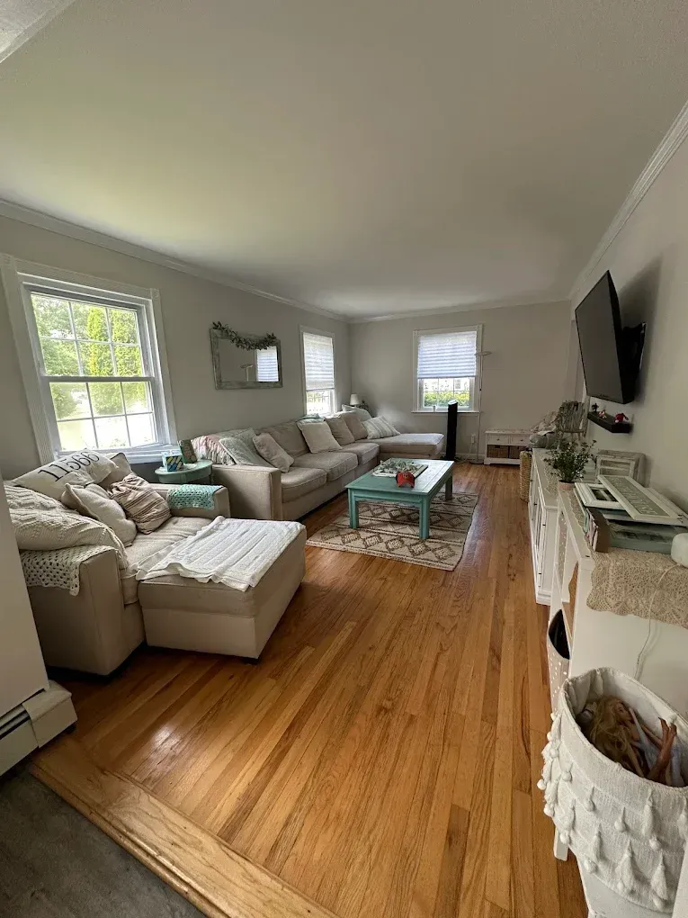 Bright living room with beige sectional, wood floors, teal coffee table, and wall-mounted TV.
