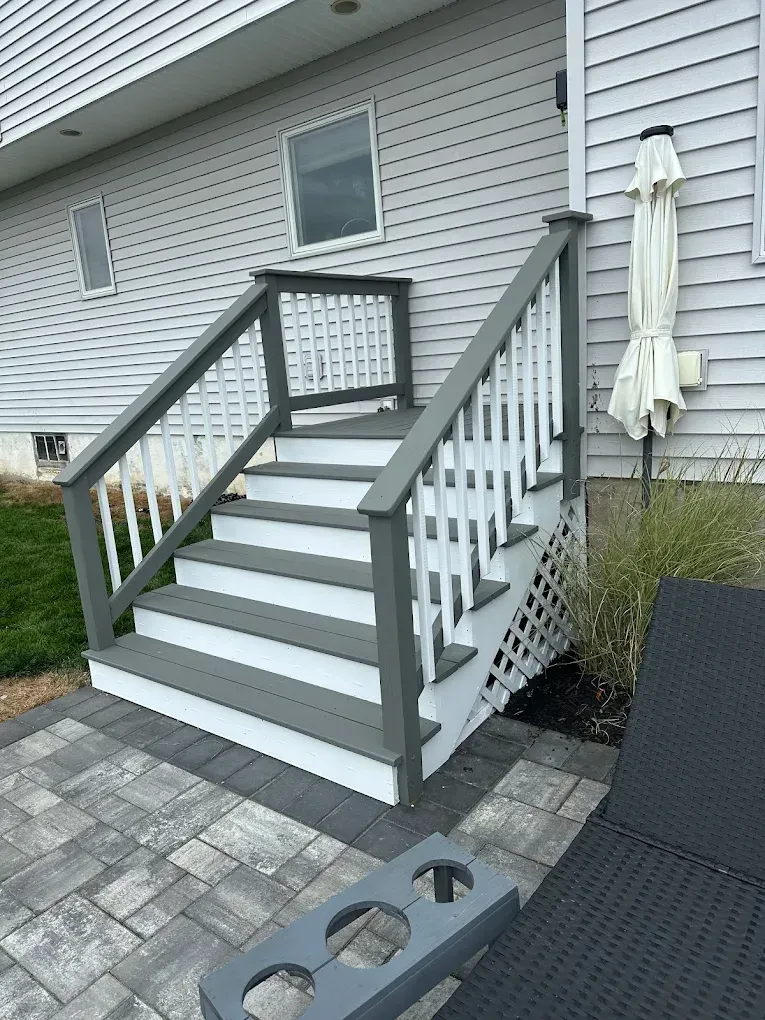 Outdoor wooden stairs with gray railings leading to a raised deck beside a house.