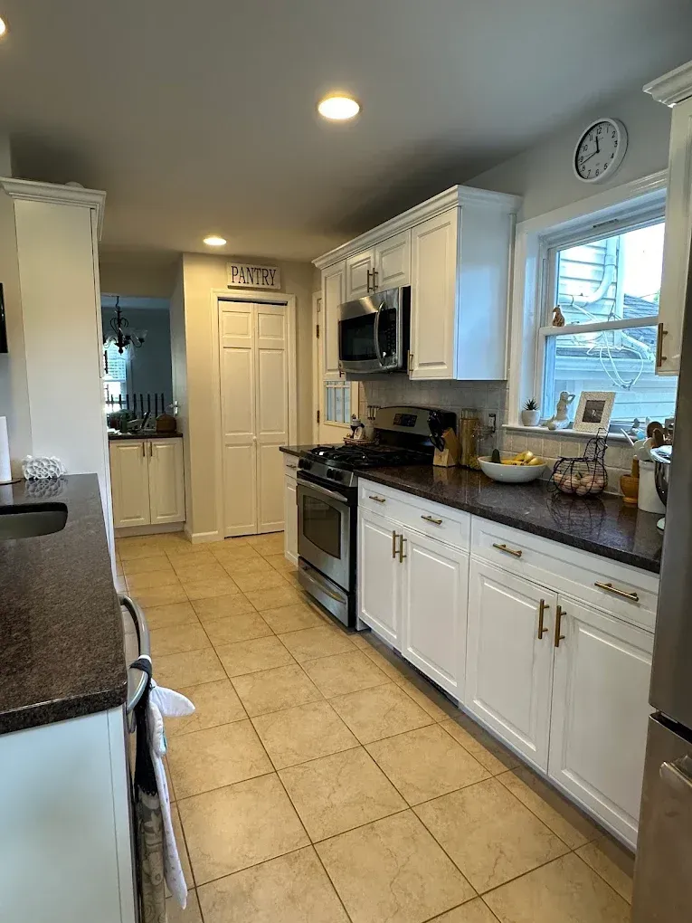 Bright kitchen with white cabinets, black countertops, tiled floor, and a window over the sink.
