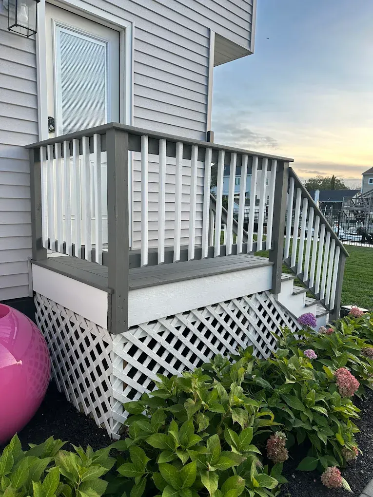 Small house deck with white railing, lattice skirt, and flowering shrubs in the foreground