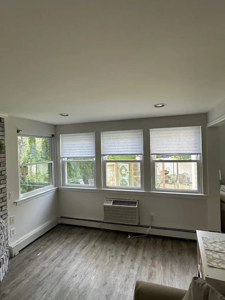 Bright empty room with large windows, gray walls, wood floors, and a radiator under the center window.