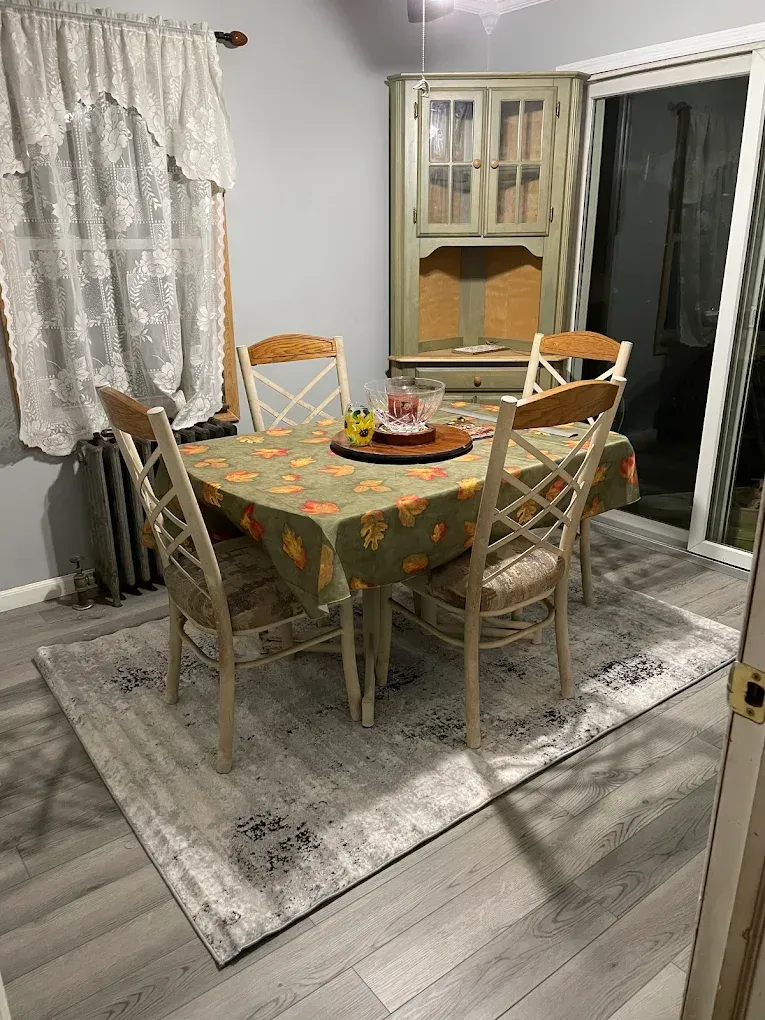 Dining room with round table, four chairs, floral tablecloth, and a fruit centerpiece by sliding glass doors.