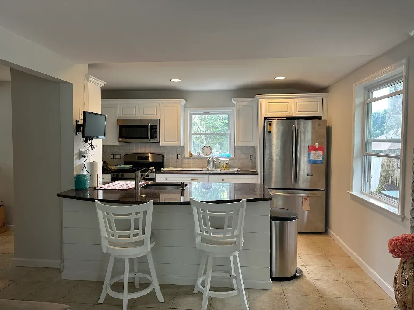 Bright modern kitchen with white cabinets, island seating, stainless fridge, and windows letting in daylight