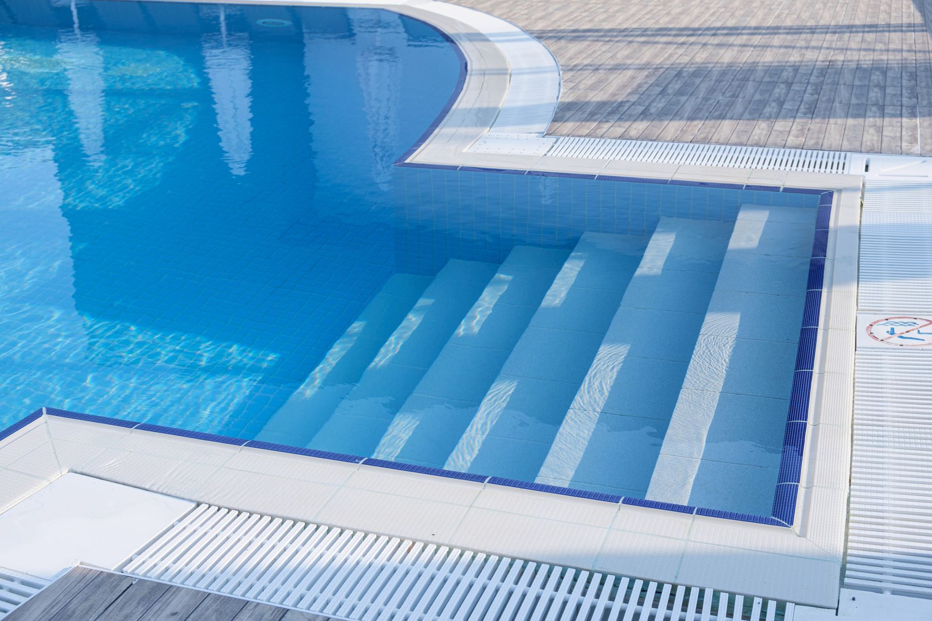 Pool with blue water and white steps. The pool's edge has a white border, and the steps descend into the water. Pool with blue water and white steps. The pool's edge has a white border, and the steps descend into the water.