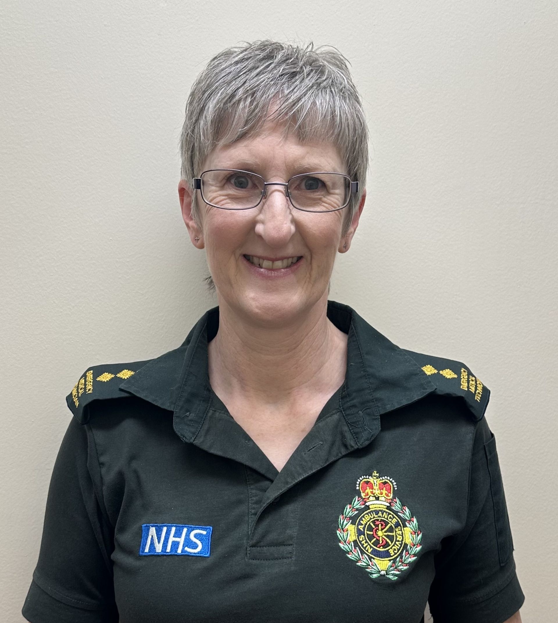 A photo of Ann who has short white hair and glasses in ambulance uniform.