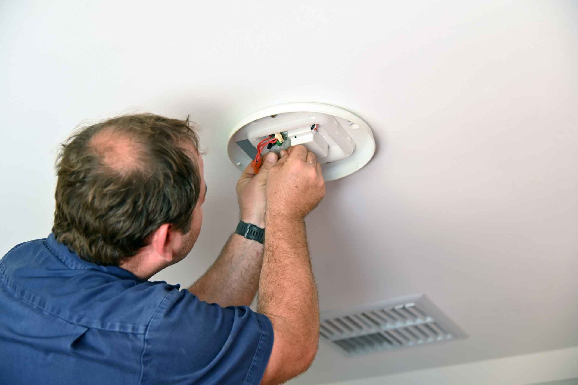 A man is fixing a light fixture on the ceiling.