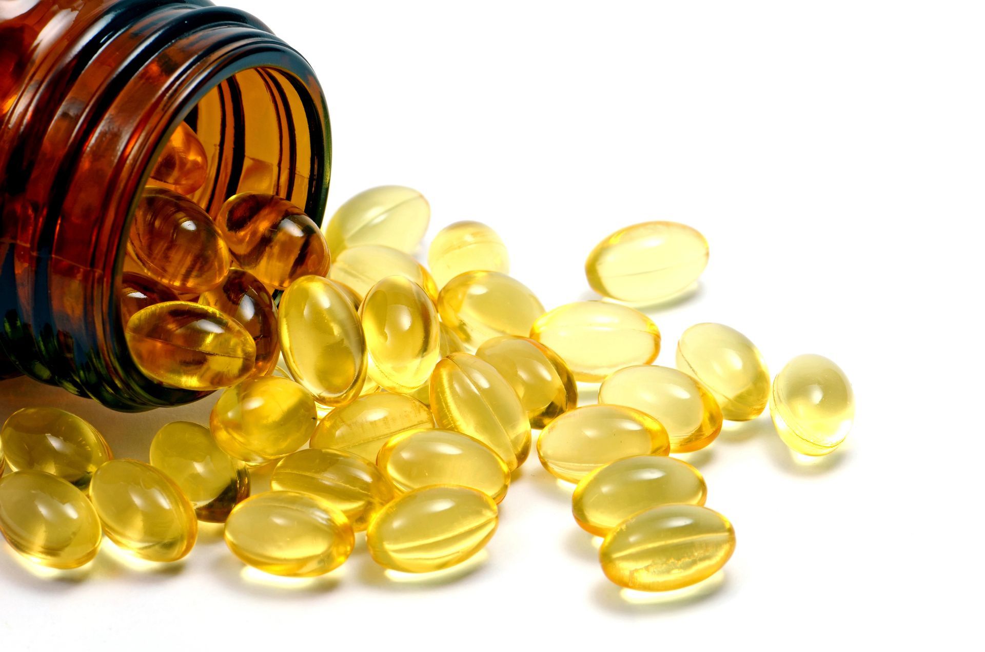 Amber glass bottle tipped over, spilling a pile of yellow, oval capsules onto a white surface.